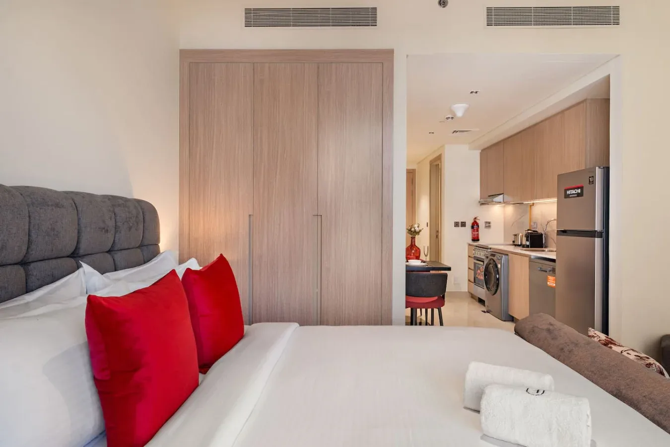 Un dormitorio con una cama y una cocina compacta visible al otro lado del tabique.