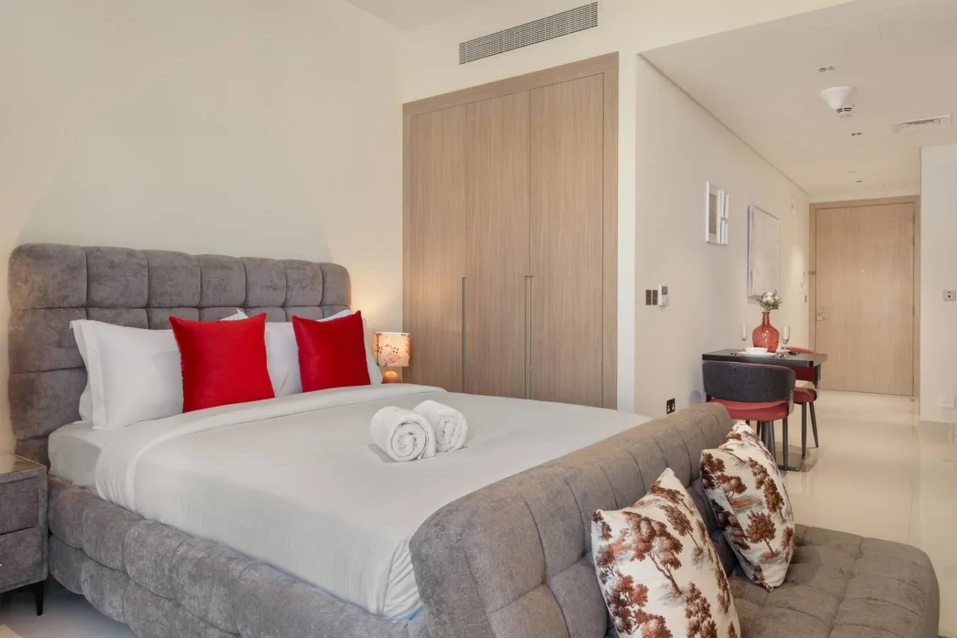 Un dormitorio con una cama grande, cojines rojos y un escritorio pequeño.