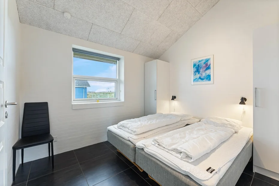Un dormitorio luminoso con dos camas, una ventana y una obra de arte en la pared.