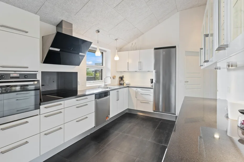 Una cocina moderna y luminosa con armarios blancos, encimeras oscuras y electrodomésticos de acero inoxidable.