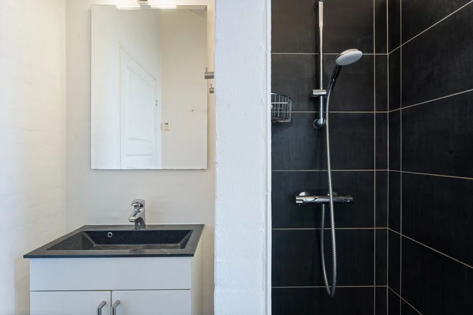 Un lavabo con mueble está junto a una ducha con azulejos oscuros.