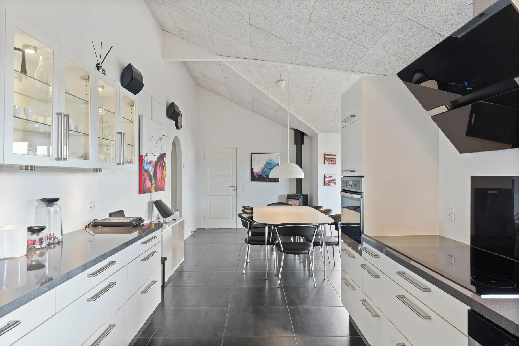 Una cocina moderna con gabinetes blancos, encimeras oscuras y una mesa de comedor.
