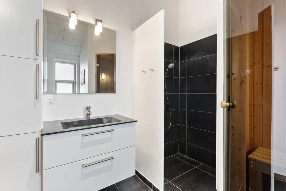 Un baño moderno con tocador y una ducha con azulejos negros.