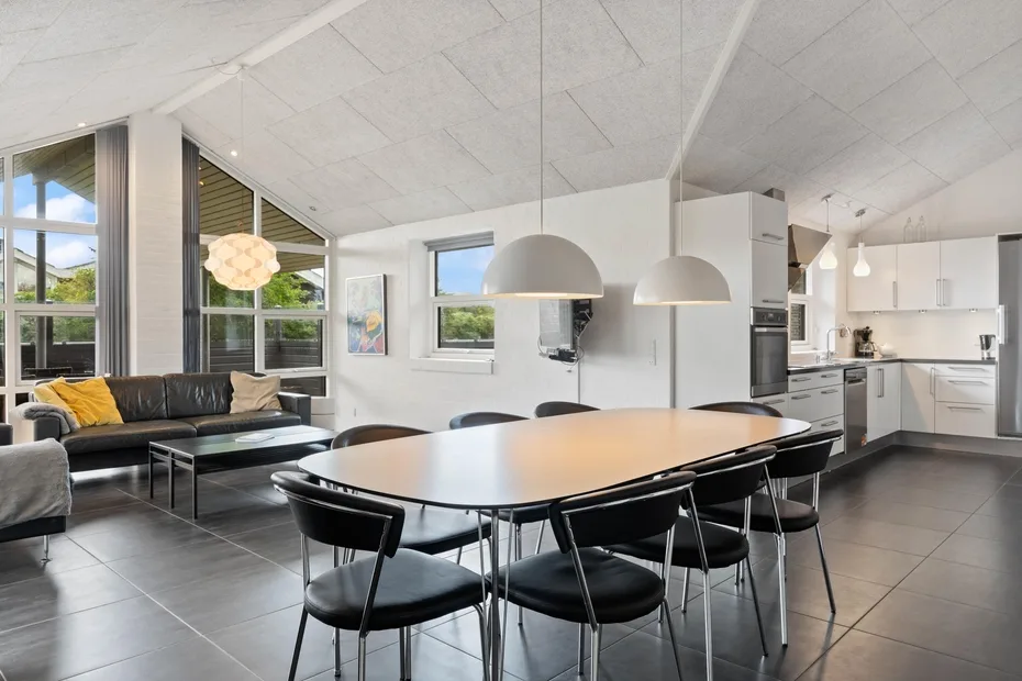 Una luminosa zona abierta de comedor y cocina con mesa, asientos y lámparas colgantes.