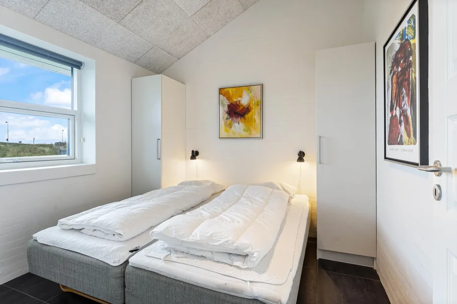 Un dormitorio luminoso con dos camas individuales y cuadros enmarcados.