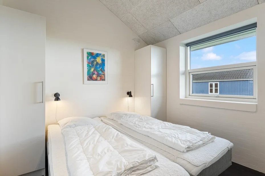 Un dormitorio luminoso con ropa de cama blanca y una obra de arte colorida en la pared.