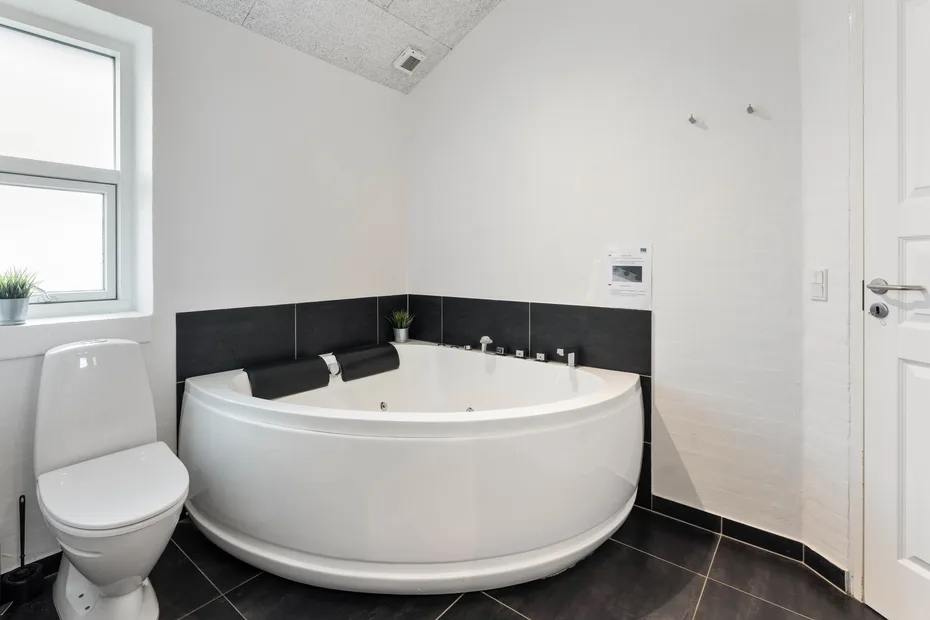 Un baño luminoso con una bañera curva, un inodoro y una ventana.