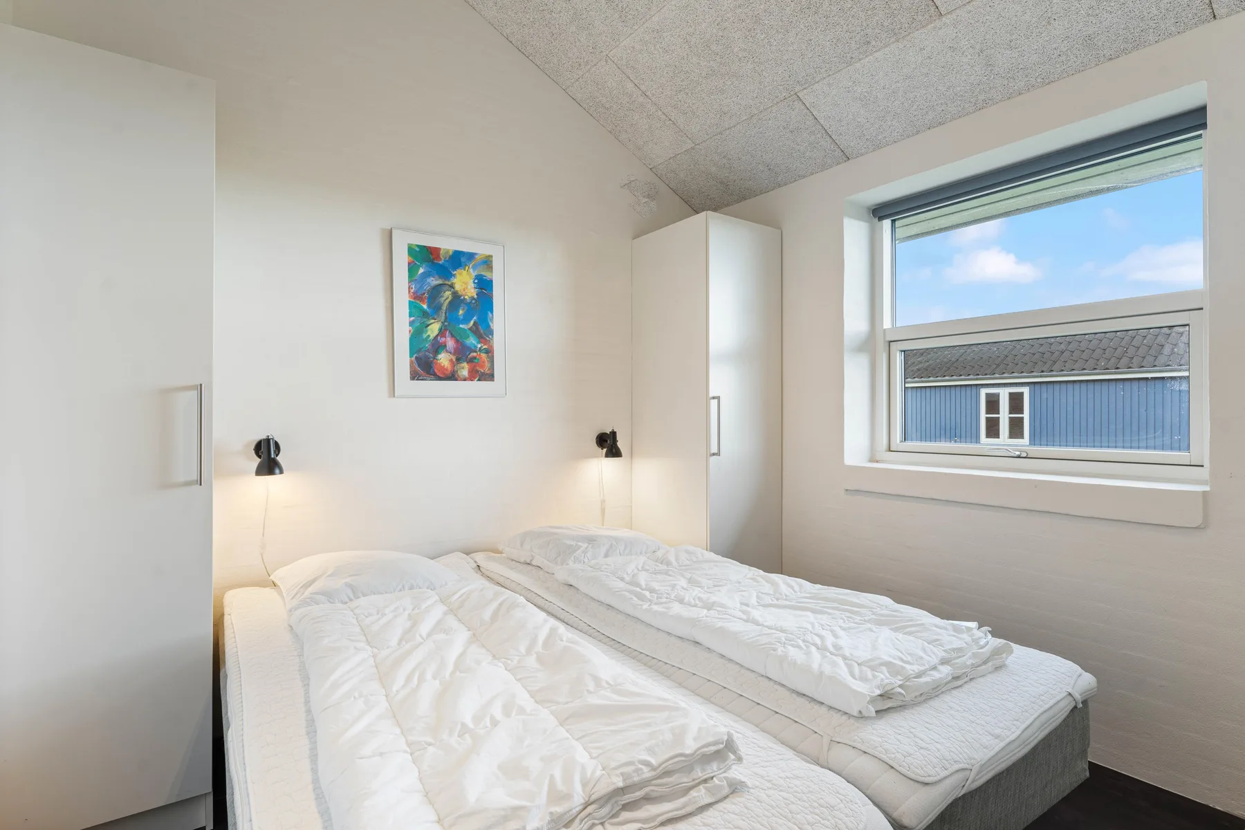 Un dormitorio luminoso con dos camas, ropa de cama blanca y arte colorido en la pared.