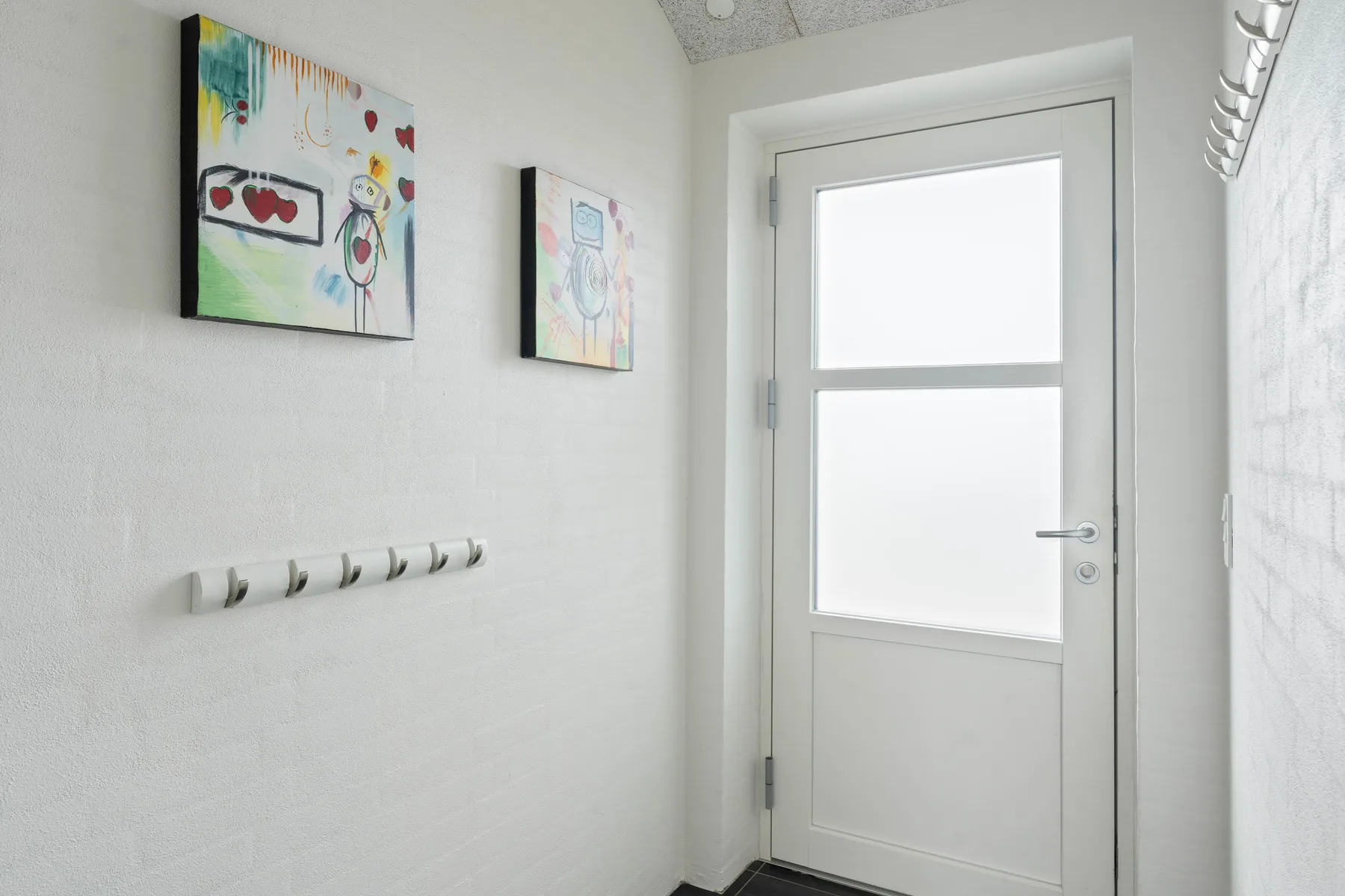 Un recibidor luminoso con una puerta blanca y cuadros coloridos en la pared.