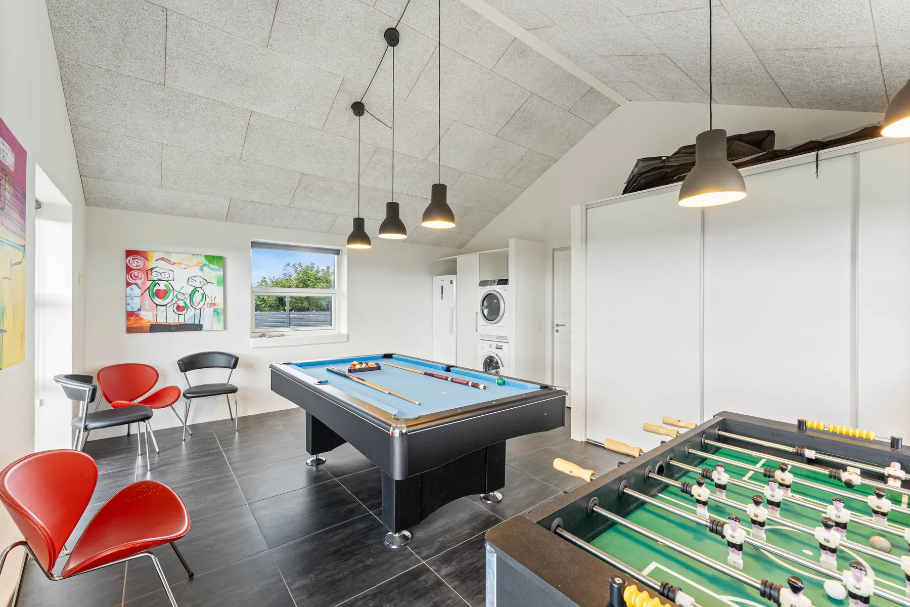 Una sala de juegos con mesa de billar, futbolín y asientos.