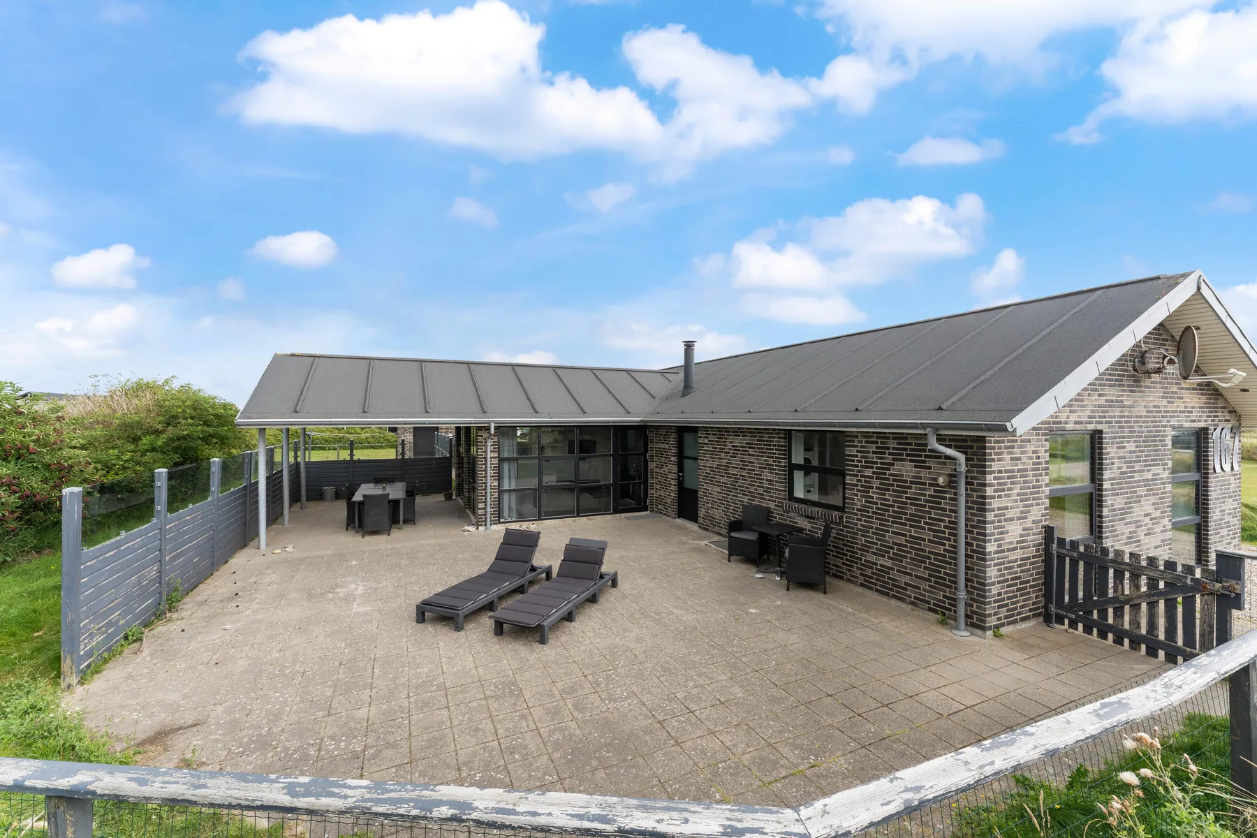 Un patio exterior pavimentado junto a una casa de ladrillo, con asientos y una mesa.