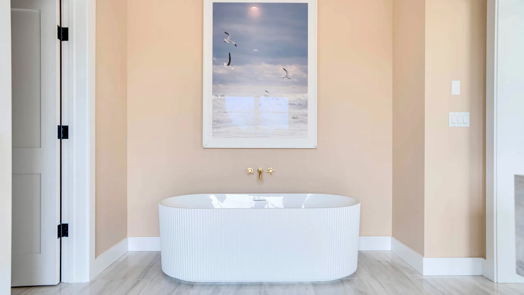 Una bañera exenta está bajo una fotografía enmarcada de la playa en un baño de tonos suaves.