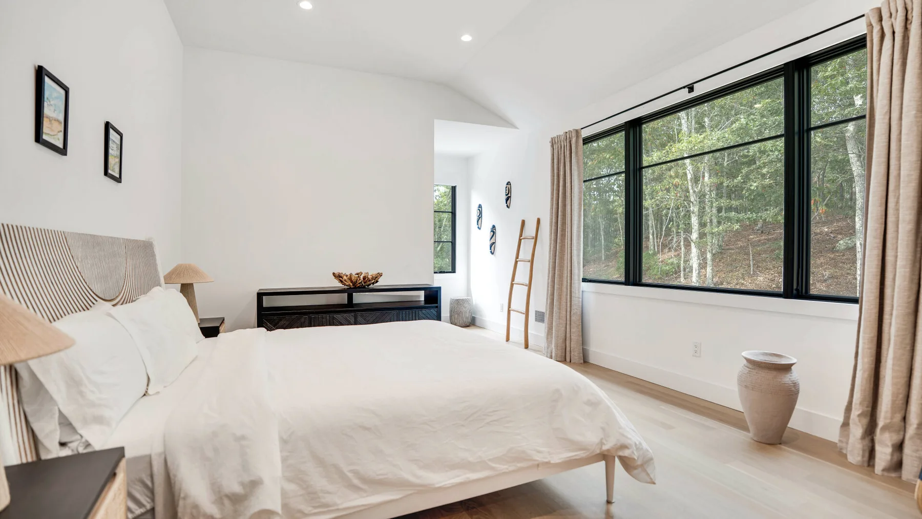 Un dormitorio luminoso con una cama grande y amplias ventanas con vista a los árboles.