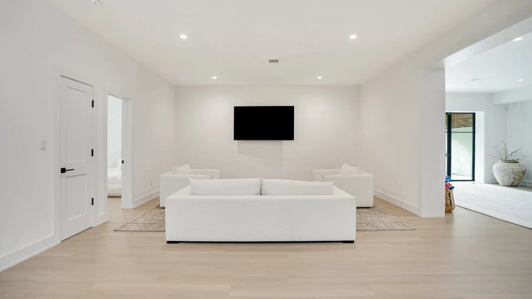 Una sala luminosa con asientos blancos y un televisor montado en la pared.