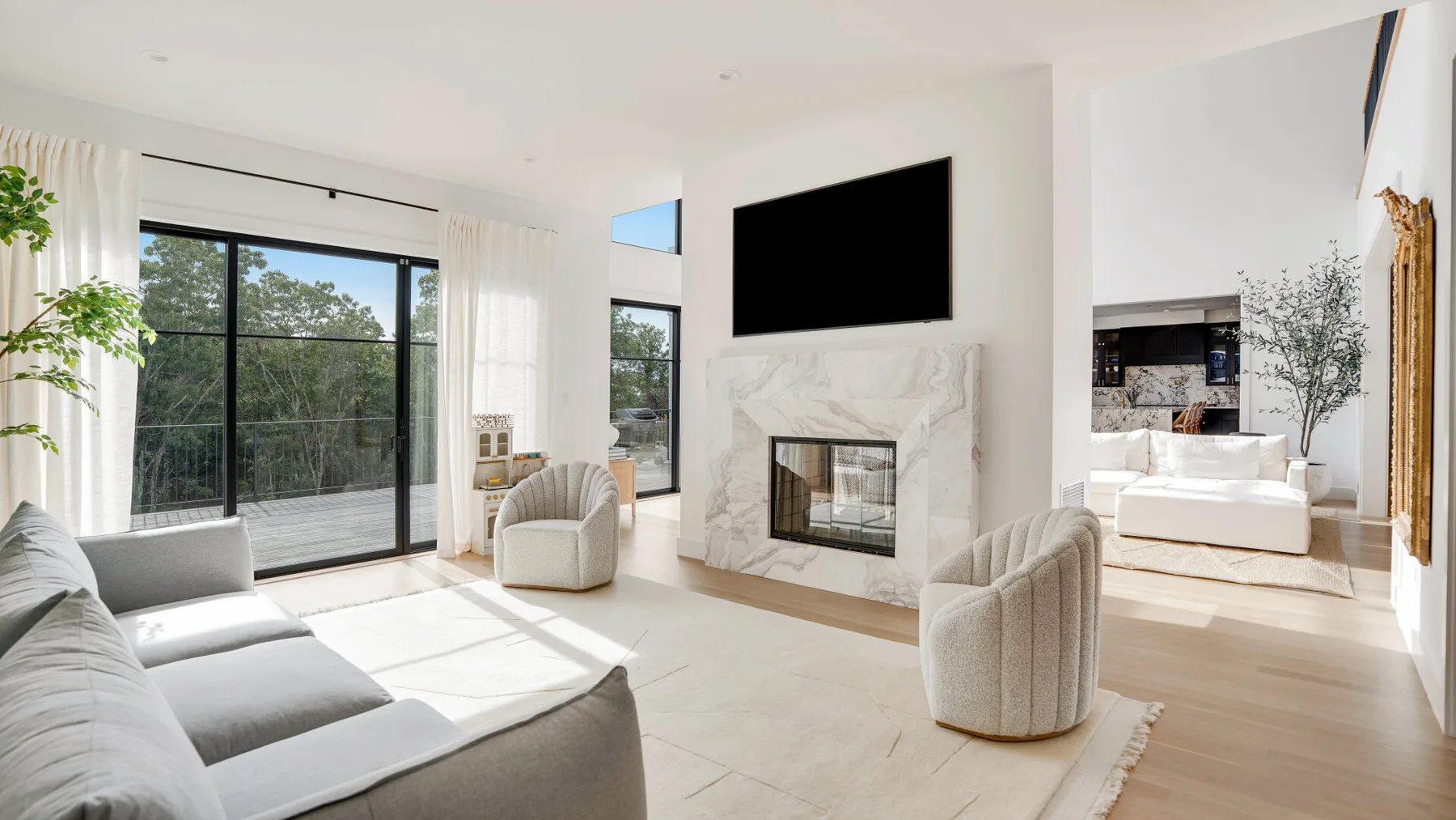 Una sala luminosa con chimenea, televisor y grandes ventanas.