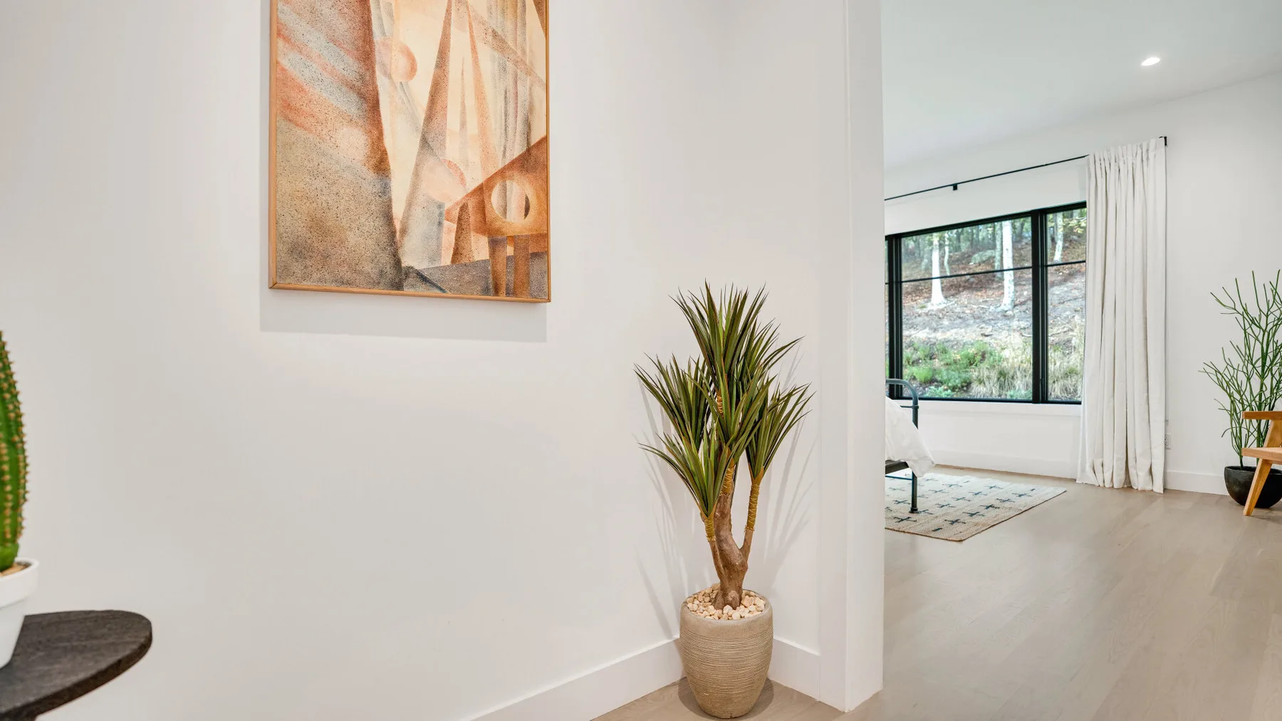 Una sala luminosa con una ventana amplia, suelo claro y plantas en macetas.