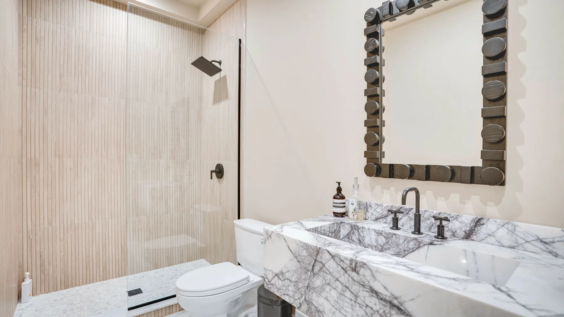 Un baño luminoso con un tocador de efecto mármol y una ducha de vidrio.