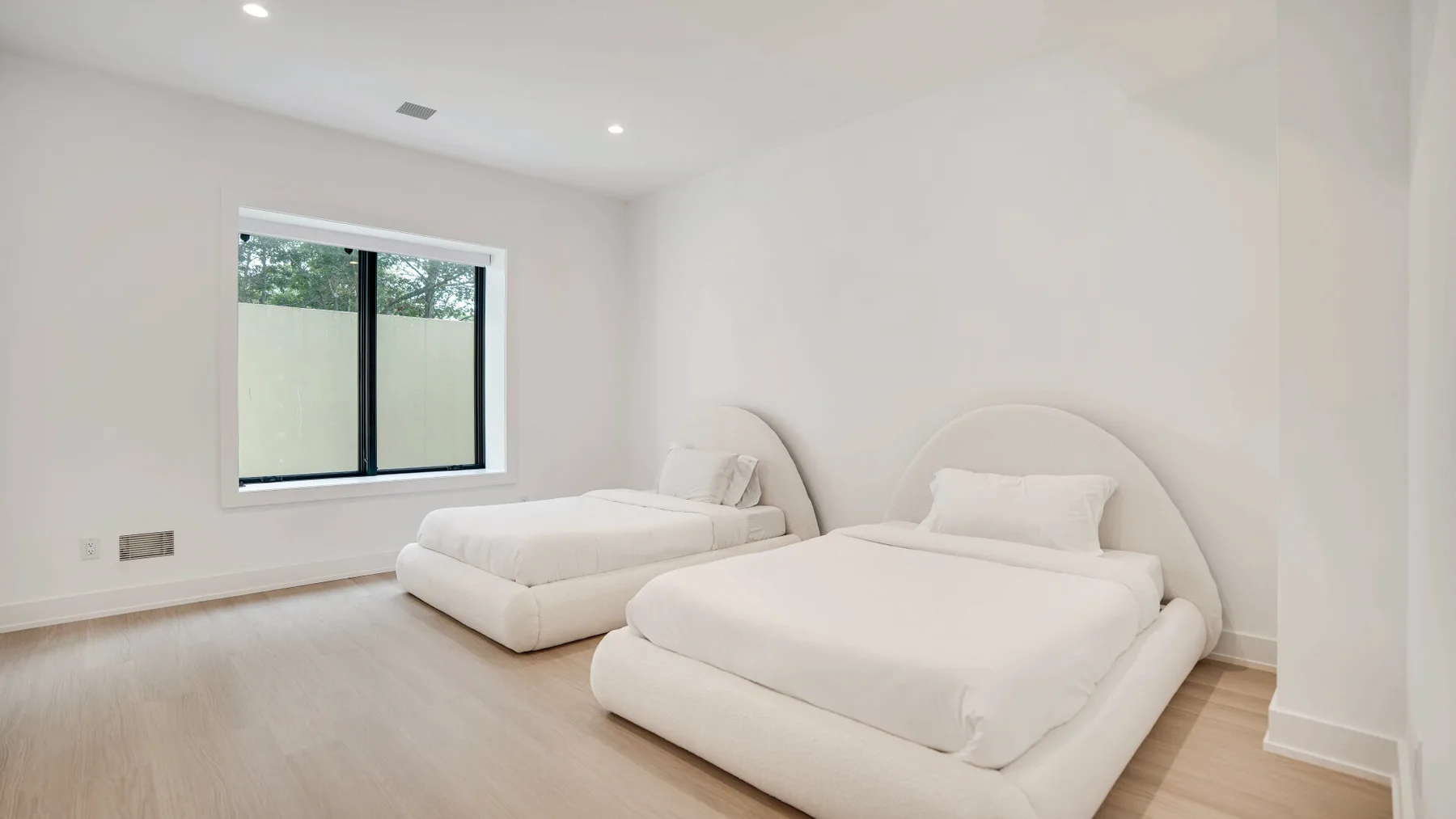 Un dormitorio luminoso con dos camas blancas y una ventana.