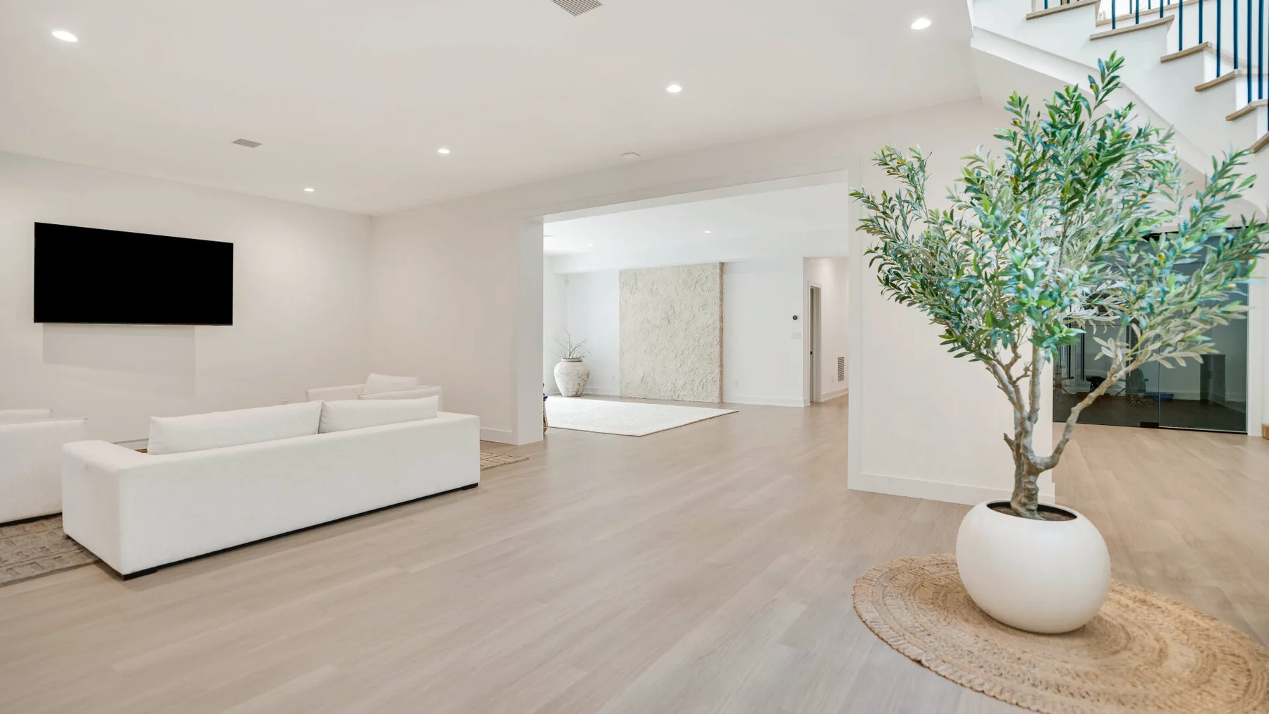 Una sala luminosa con asientos blancos y un árbol en maceta junto a la escalera.