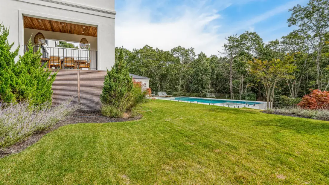 A landscaped lawn beside a house with an elevated deck and swimming pool.