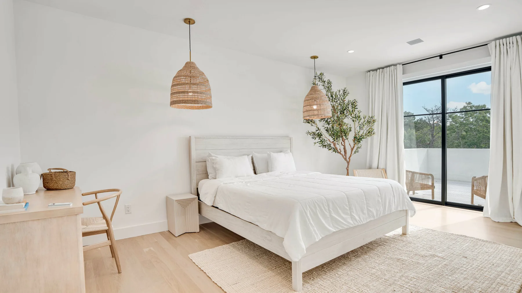 Un dormitorio luminoso con una cama blanca junto a una gran puerta de vidrio.