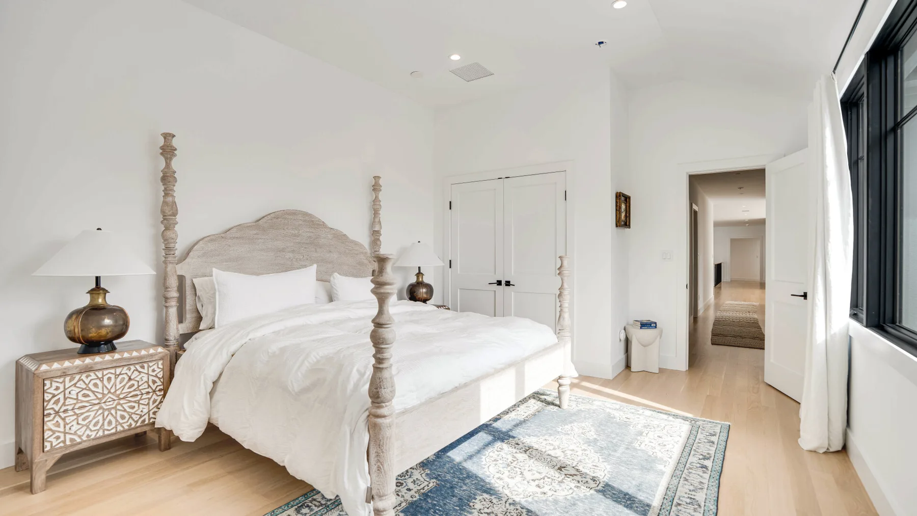 Un dormitorio luminoso cuenta con una cama blanca, mesitas de noche y una alfombra estampada.