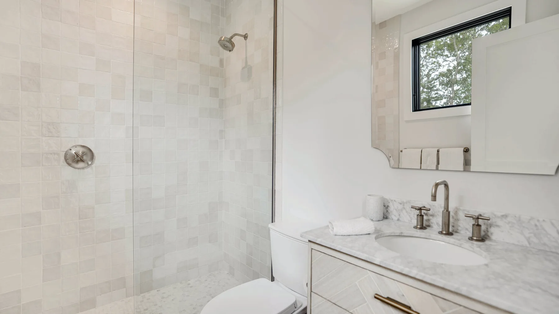 Un baño luminoso con una ducha alicatada y un lavabo bajo una ventana.