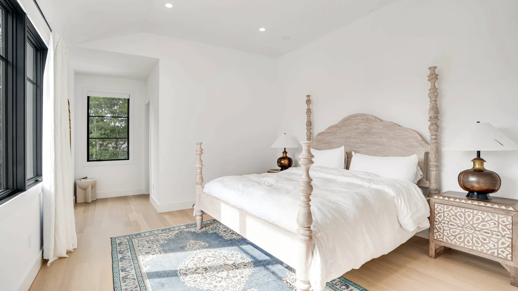 Un dormitorio luminoso con una cama con dosel y una alfombra estampada.