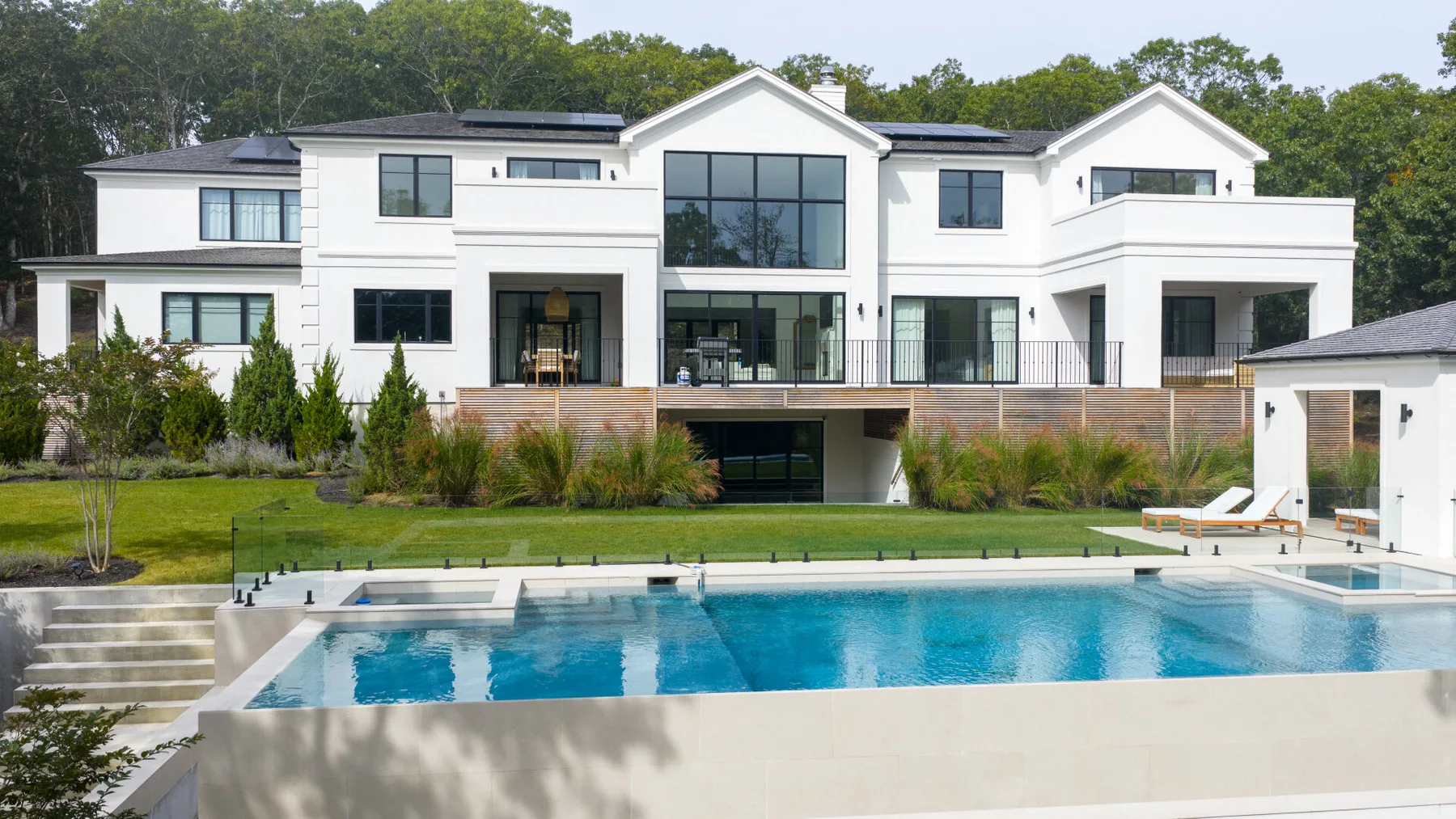 A modern white house overlooks a swimming pool and landscaped lawn.