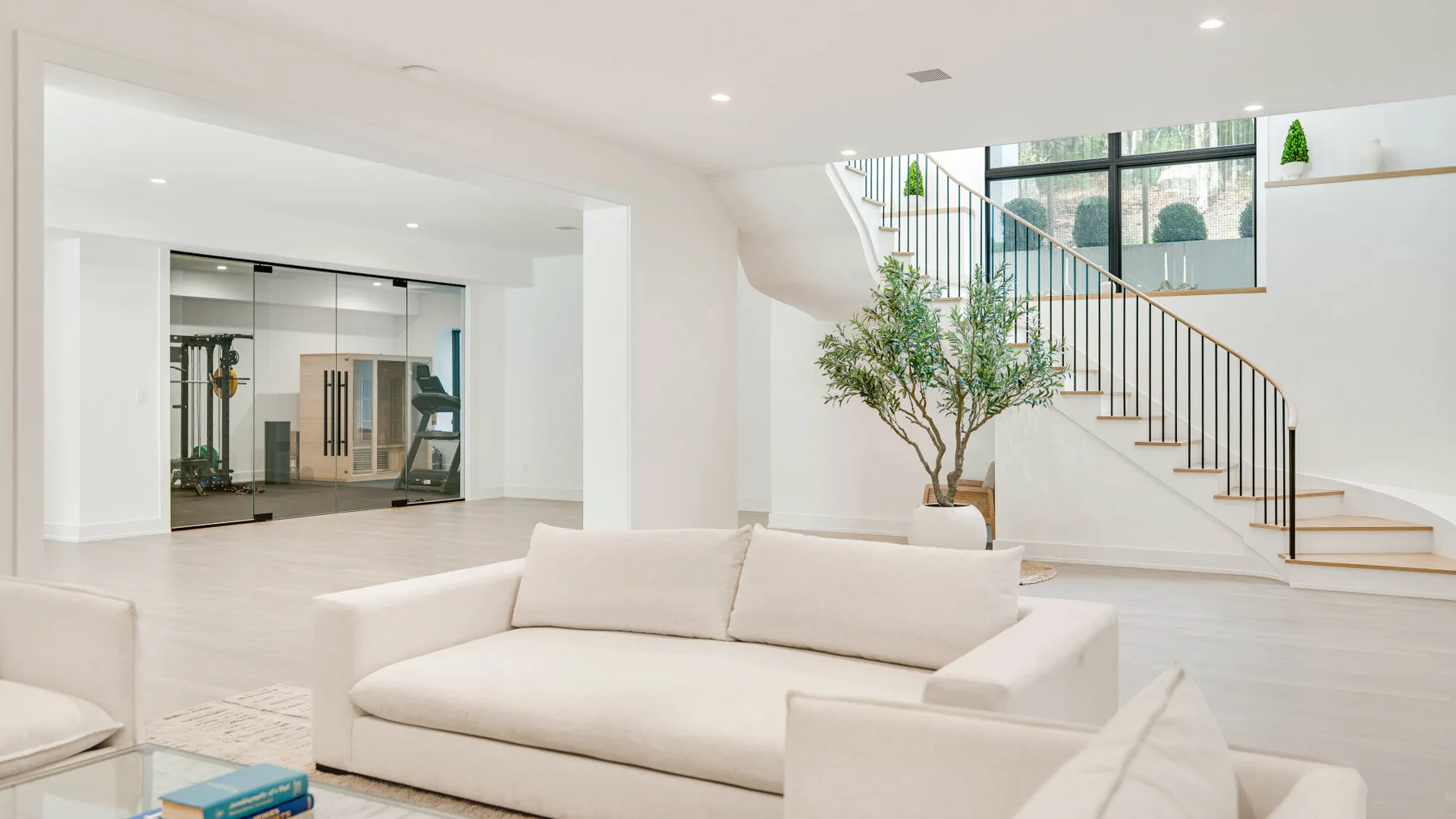Una sala luminosa con asientos claros y una escalera junto a un árbol pequeño.