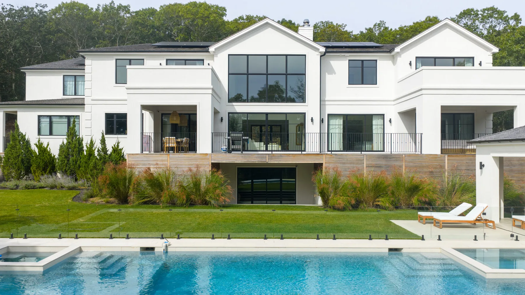 Una gran casa blanca moderna se alza detrás de una piscina y un jardín ajardinado.