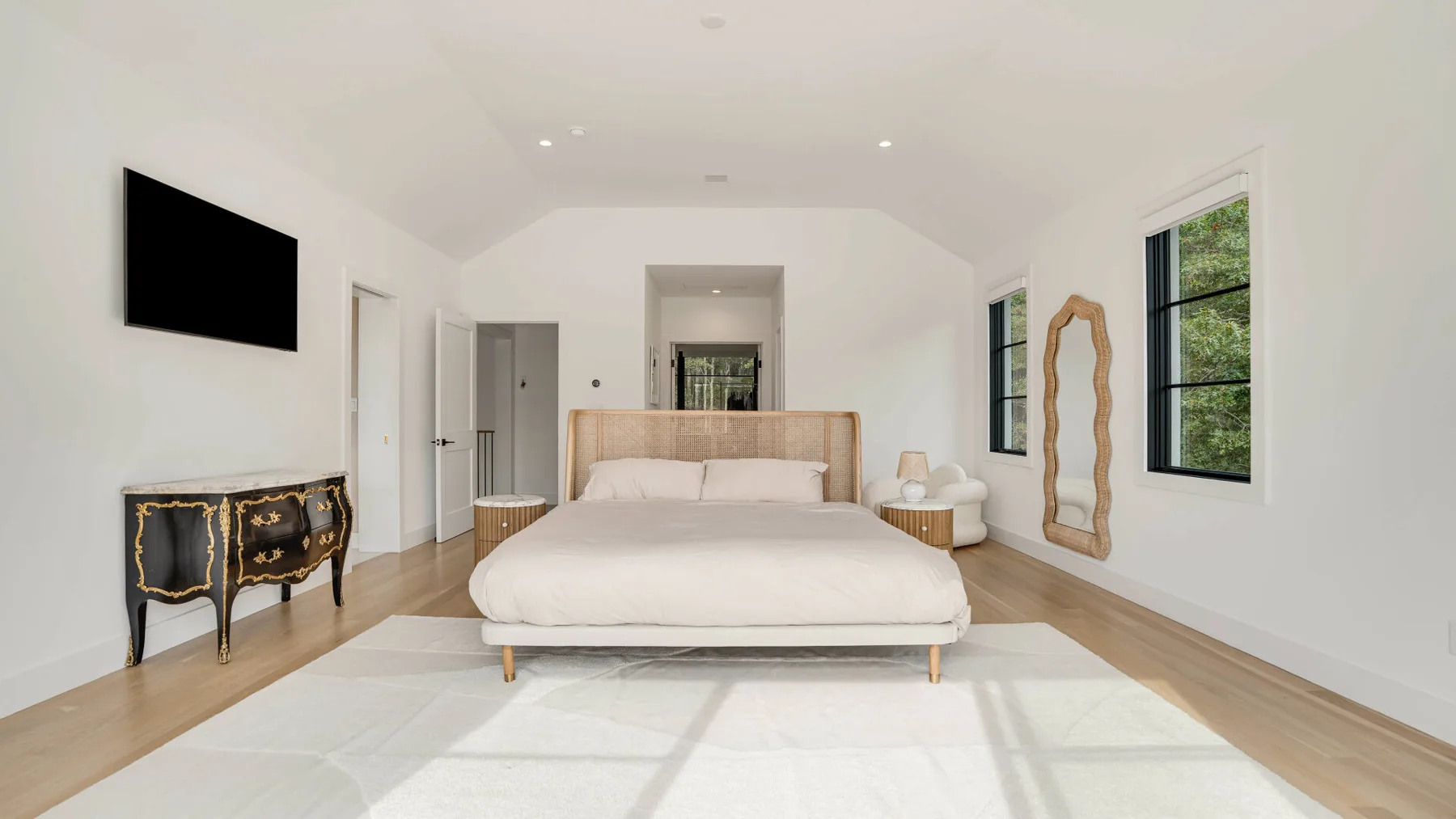 Un dormitorio luminoso con una cama, un televisor en la pared y ventanas.