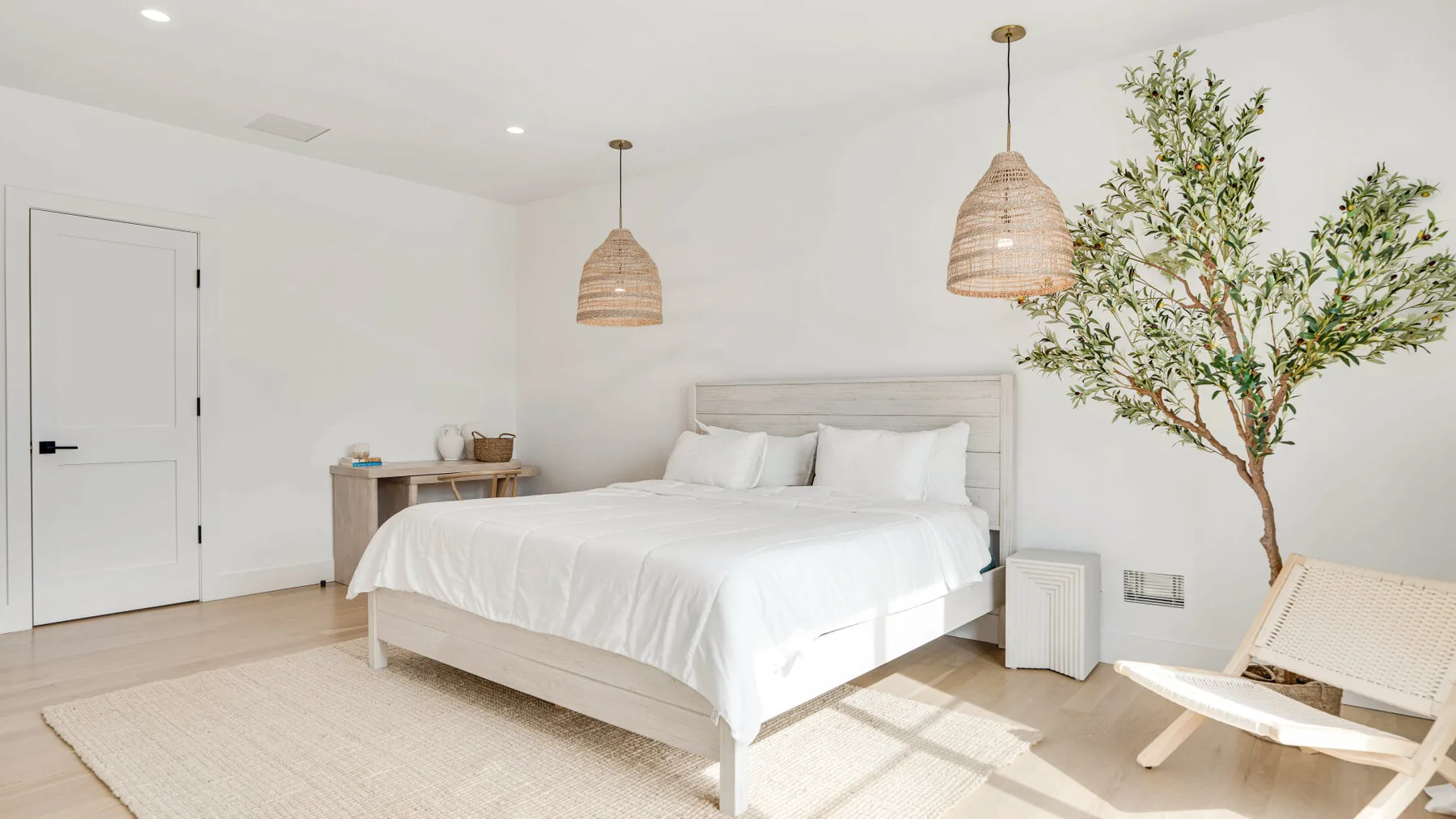 Un dormitorio luminoso con una cama bien tendida y un árbol de interior frondoso.