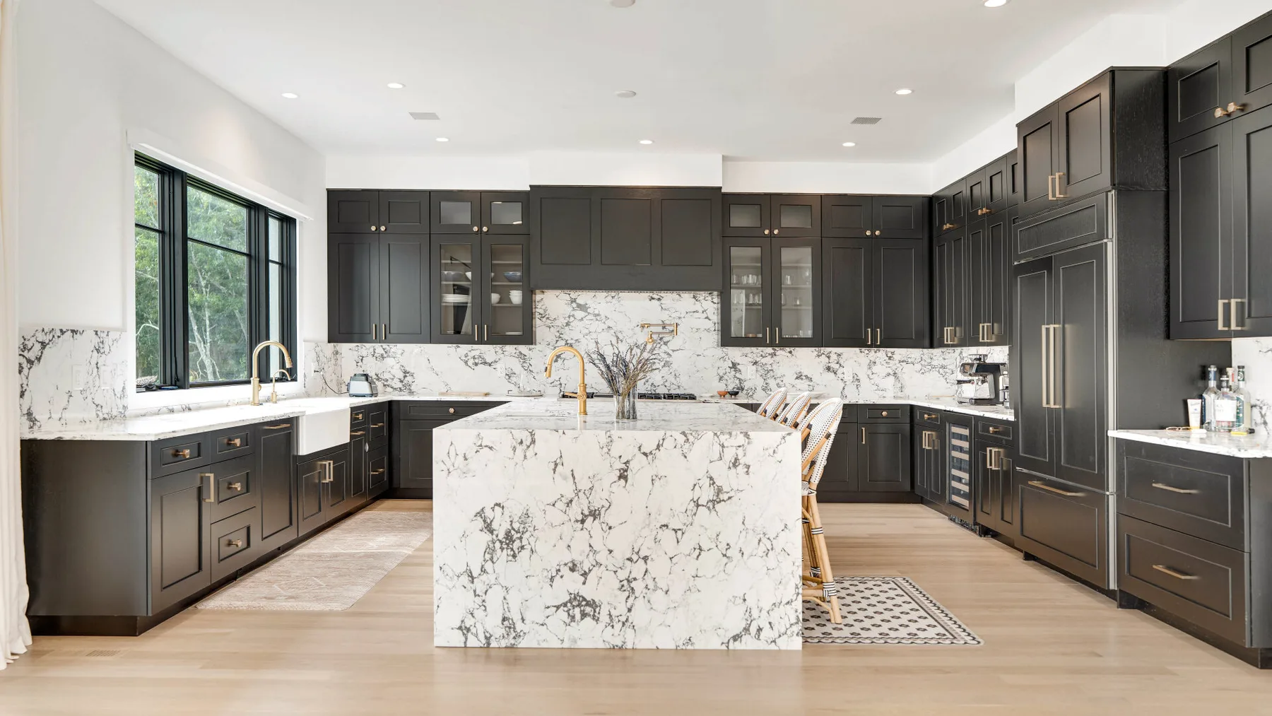 Una cocina luminosa con gabinetes oscuros y una gran isla de piedra veteada.