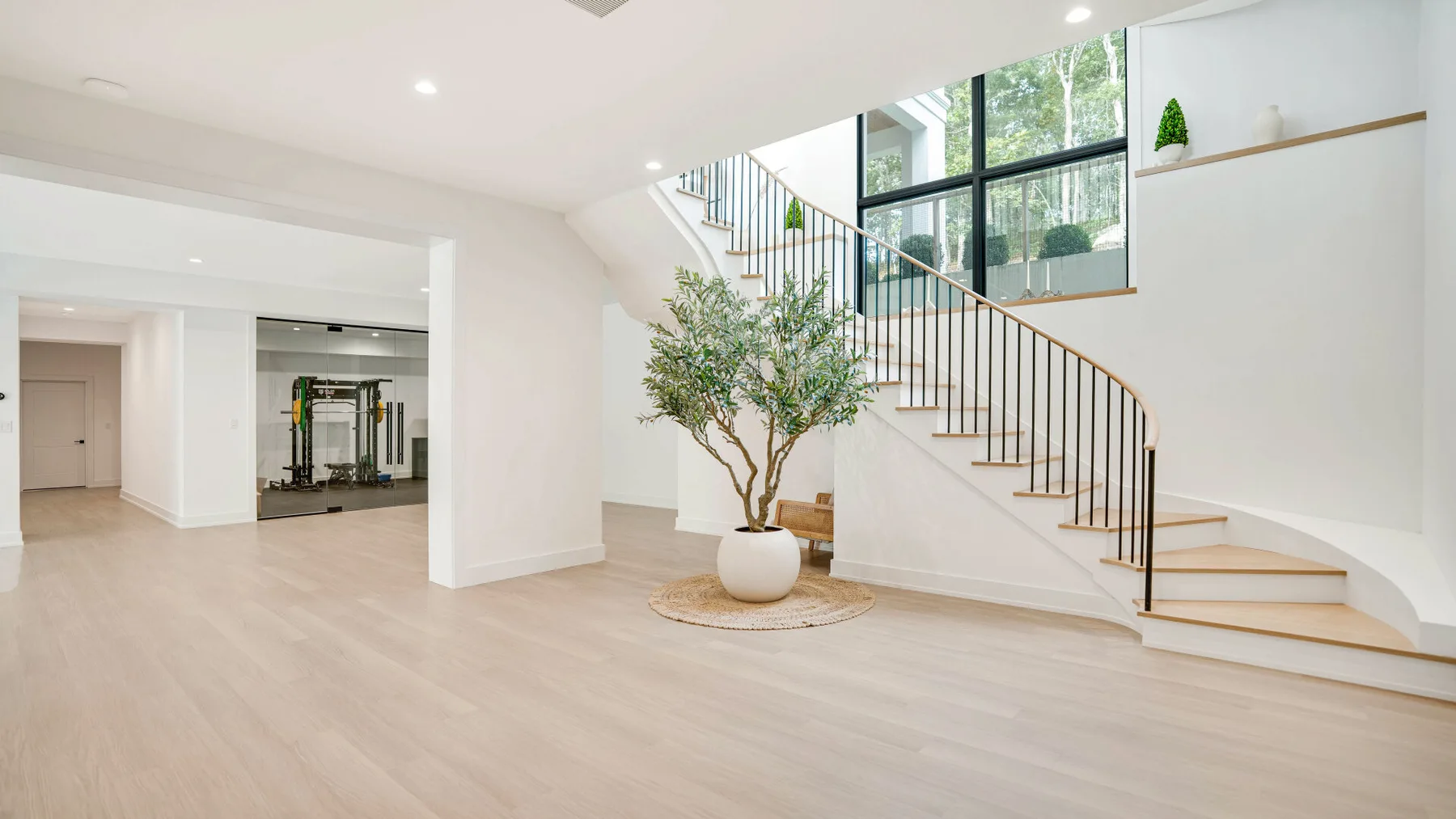 Un interior amplio y luminoso con una escalera curva y un árbol en maceta.