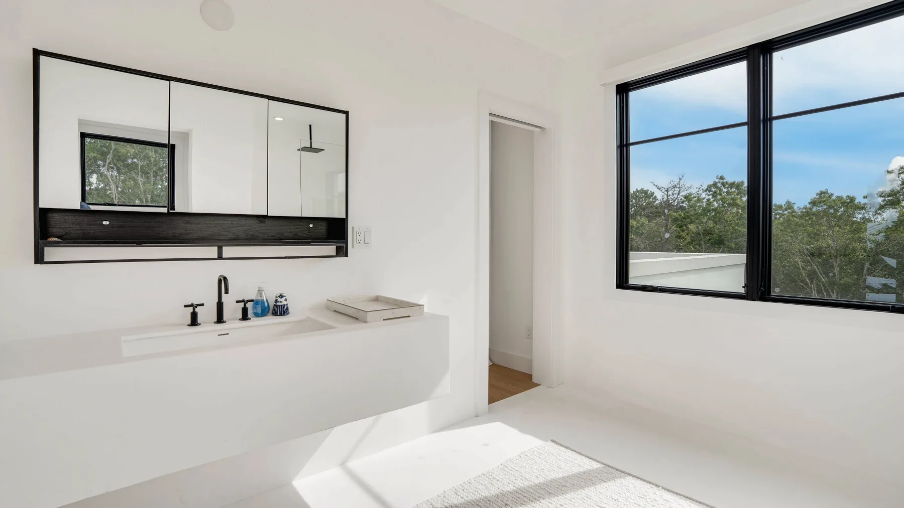 Un baño luminoso con un lavabo amplio y una gran ventana con vistas a los árboles.