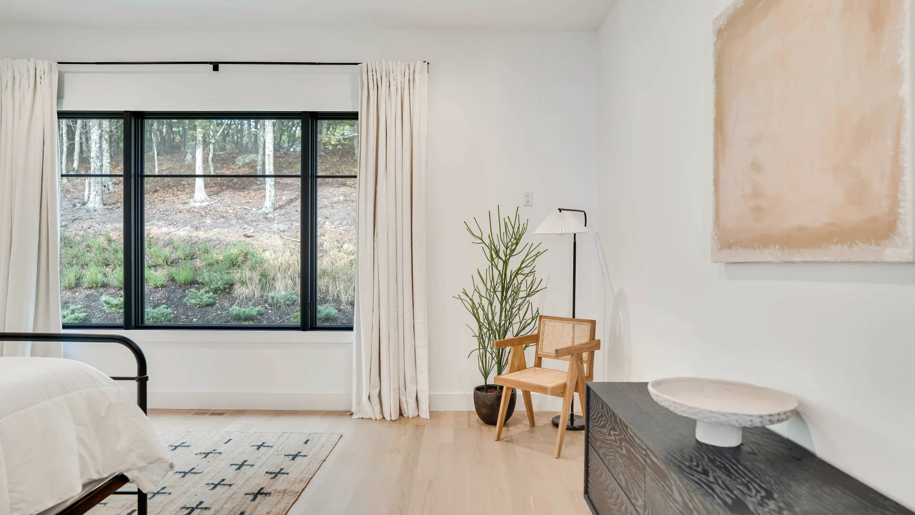 Un dormitorio luminoso con una ventana grande, una mesa auxiliar y una silla.