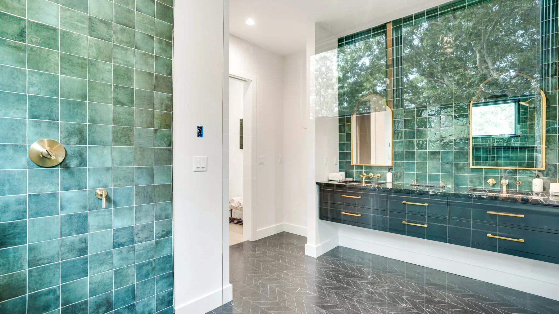 Un baño con paredes de azulejos verdes, un tocador largo y grandes ventanas.