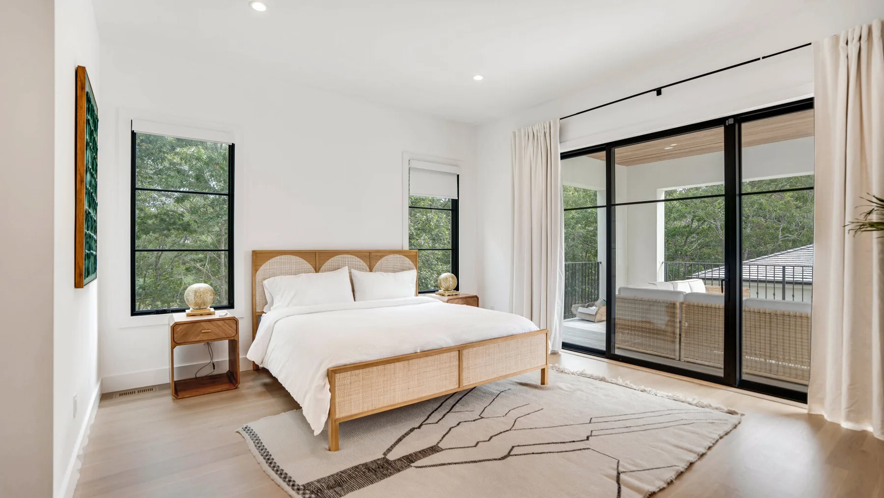 Un dormitorio luminoso con una cama junto a grandes ventanas y puertas de cristal.