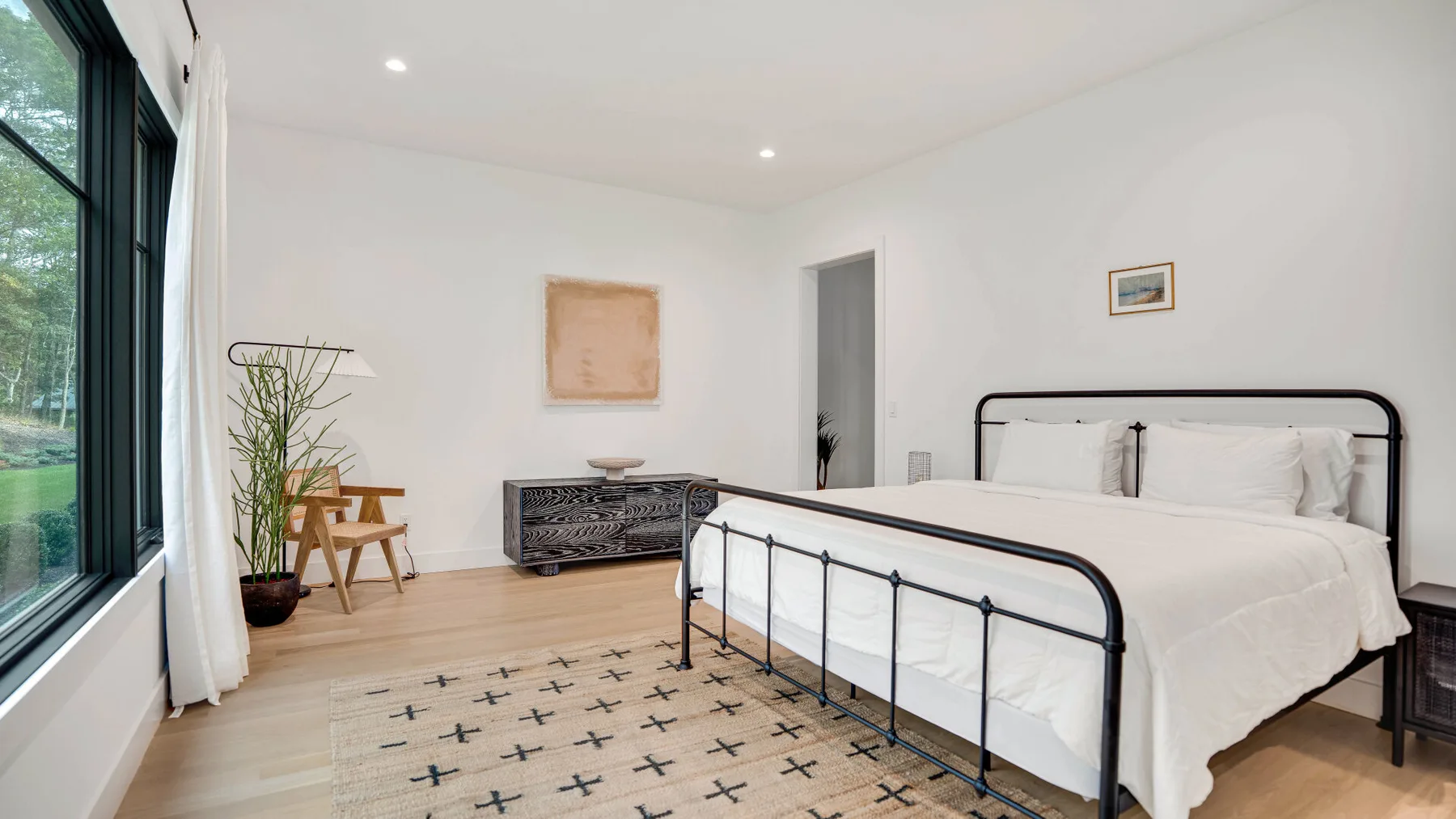 Un dormitorio luminoso con una cama de metal negro y una ventana grande.