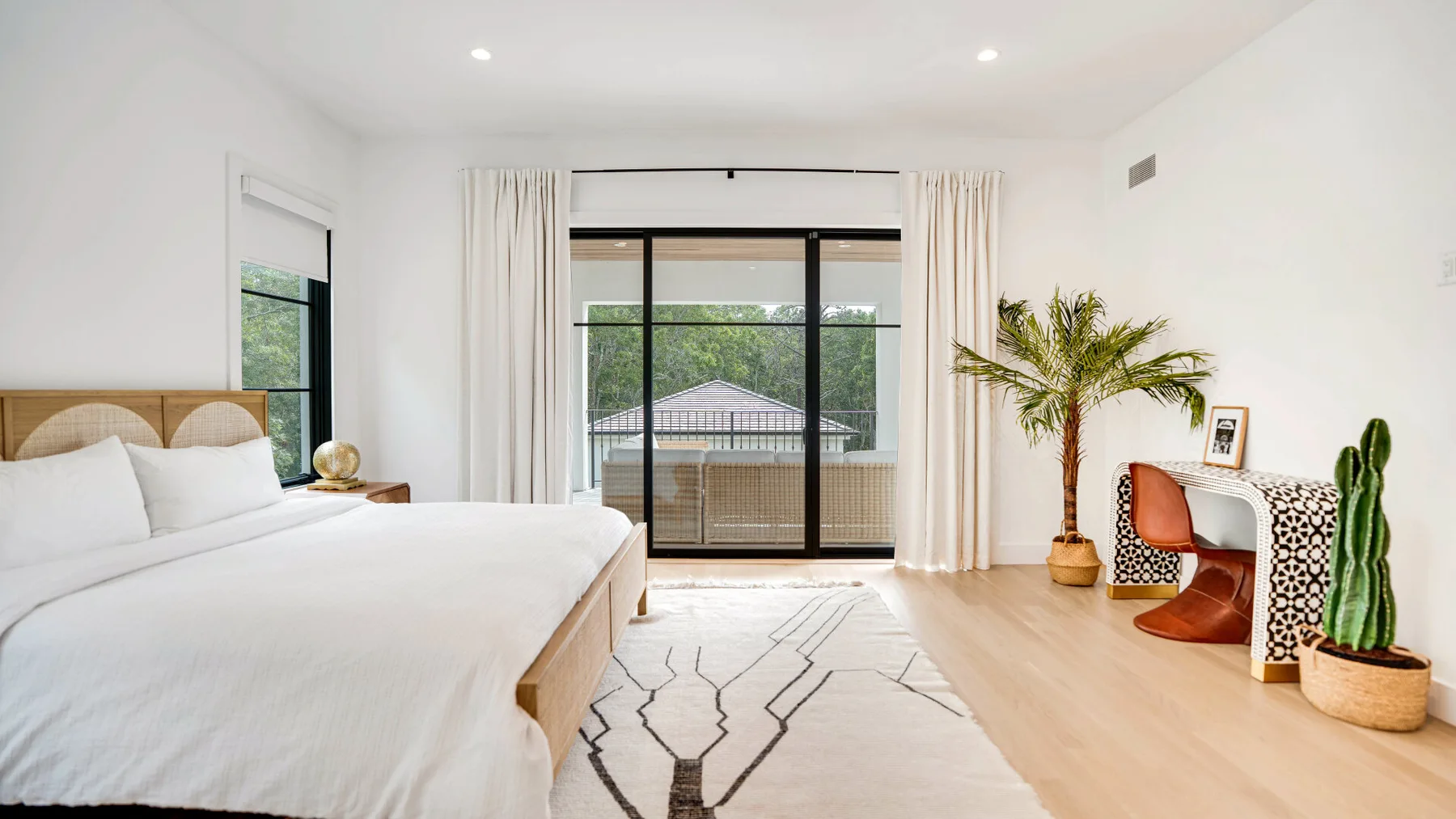 Un dormitorio luminoso con una cama grande, puertas corredizas de vidrio y plantas en macetas.