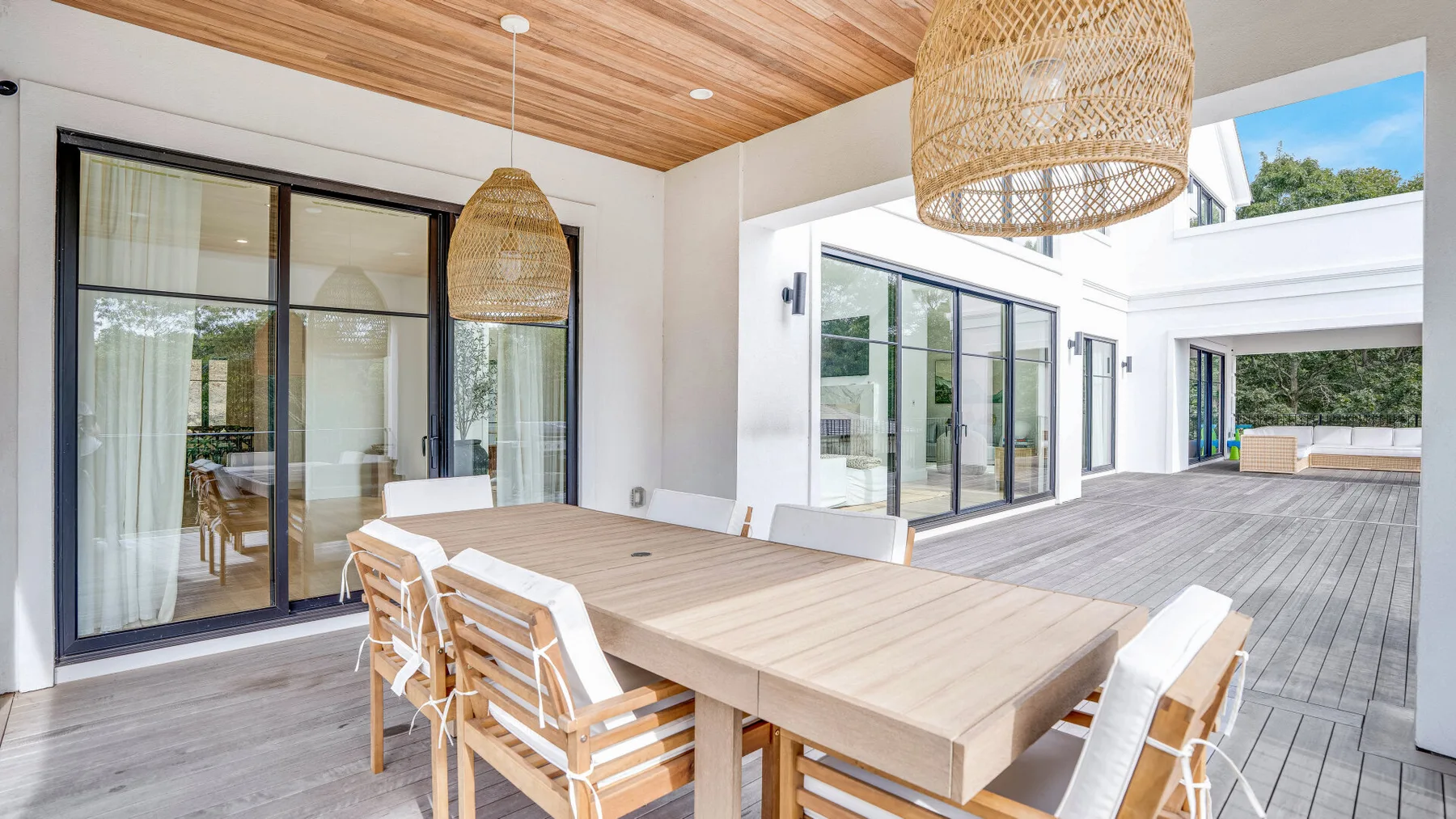 Comedor exterior cubierto con una mesa larga y lámparas colgantes tejidas.