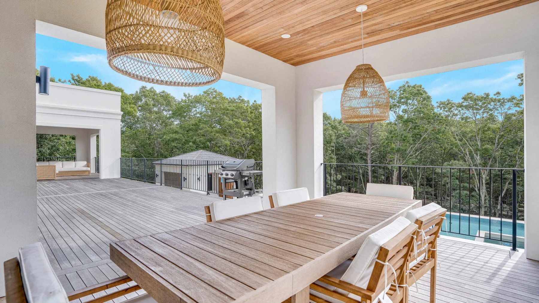 A covered outdoor dining area opens onto a deck with a view of trees.