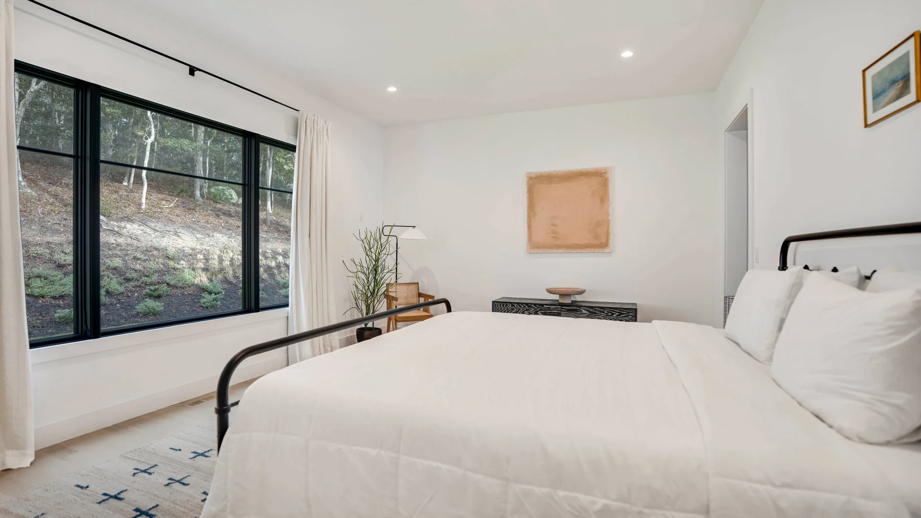 Un dormitorio luminoso con una cama grande junto a amplias ventanas con vista a los árboles.