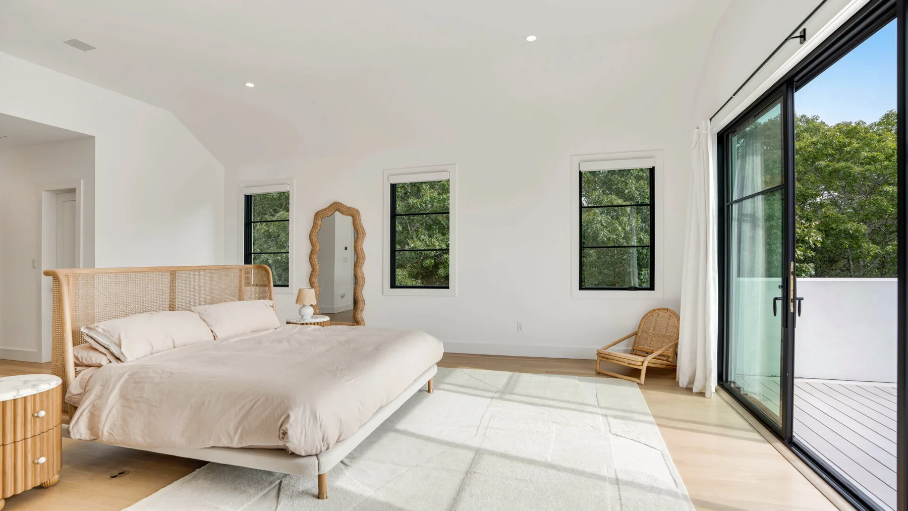Un dormitorio luminoso con una cama junto a grandes puertas de vidrio que dan a un balcón.