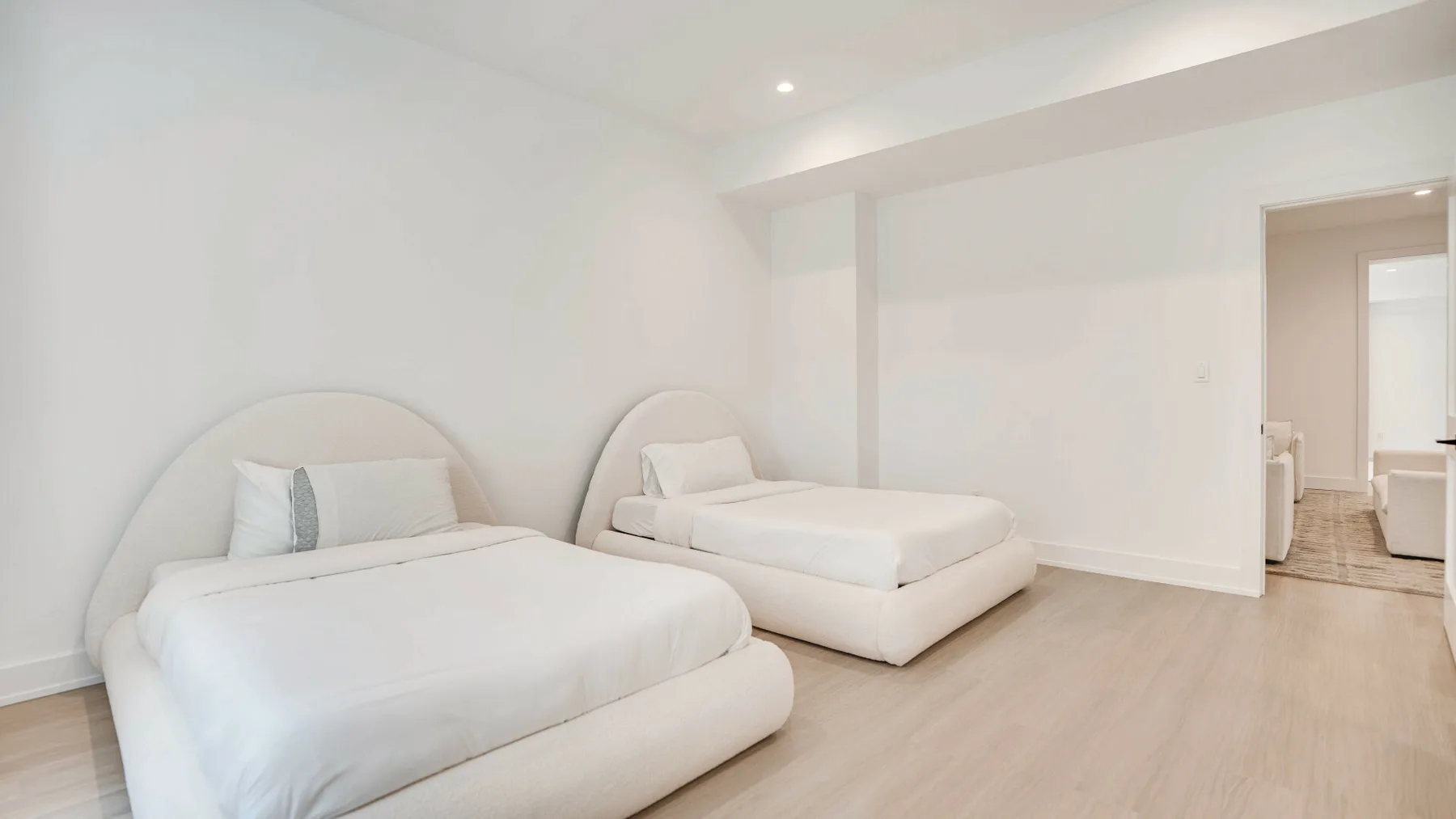 Un dormitorio luminoso con dos camas y suelo de color claro.