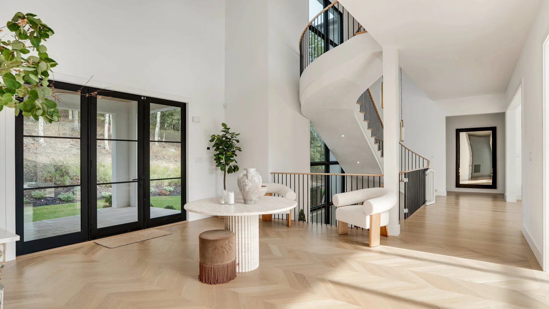 Una sala luminosa cuenta con una escalera curva y grandes puertas de vidrio.