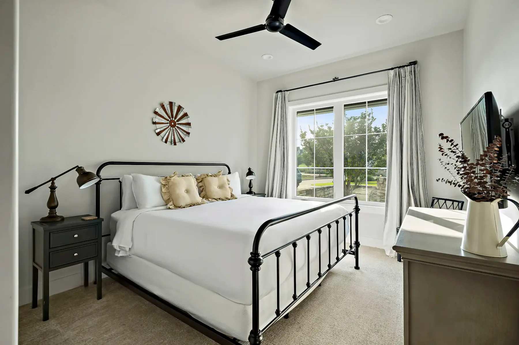 A bright bedroom with a black metal bed, white bedding, and a large curtained window.