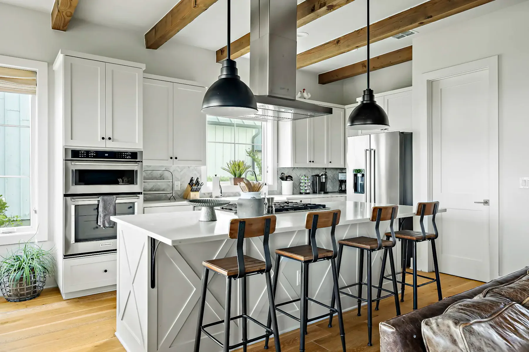 Modern kitchen with white cabinets, wooden beams, sleek appliances, an island with four barstools, and pendant lights.