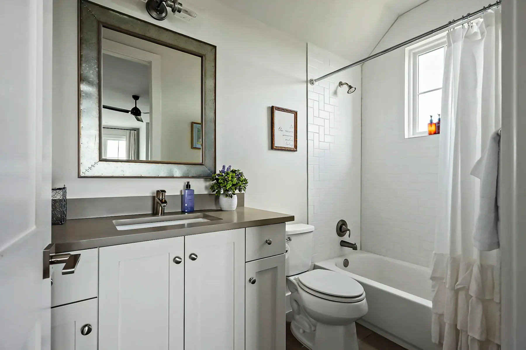 A bright bathroom has a white vanity, a large mirror, and a curtained bathtub.
